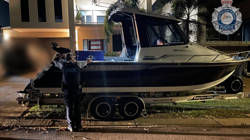 A boat on a suburban street in Darwin with an investigator inspecting the inside of the vessel.