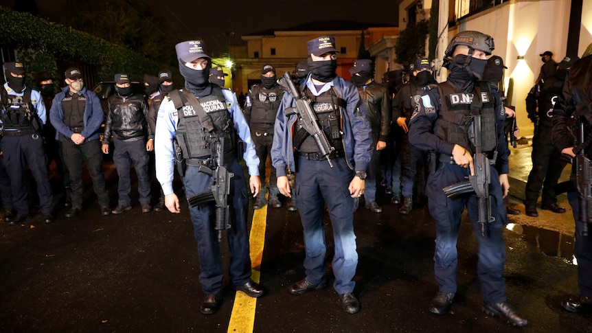 Armed special forces police wear armour and face masks as they gather on a road in the night.