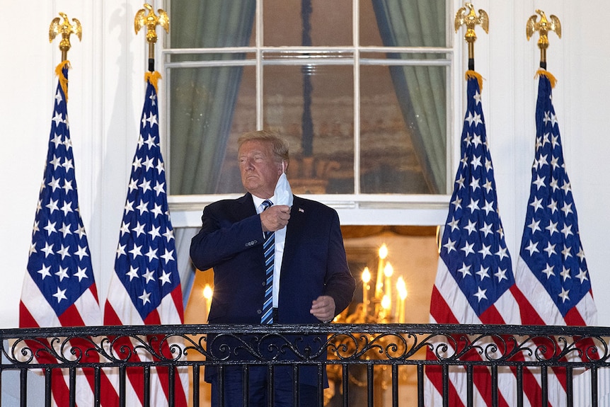 Donald Trump removing mask on White House balcony.