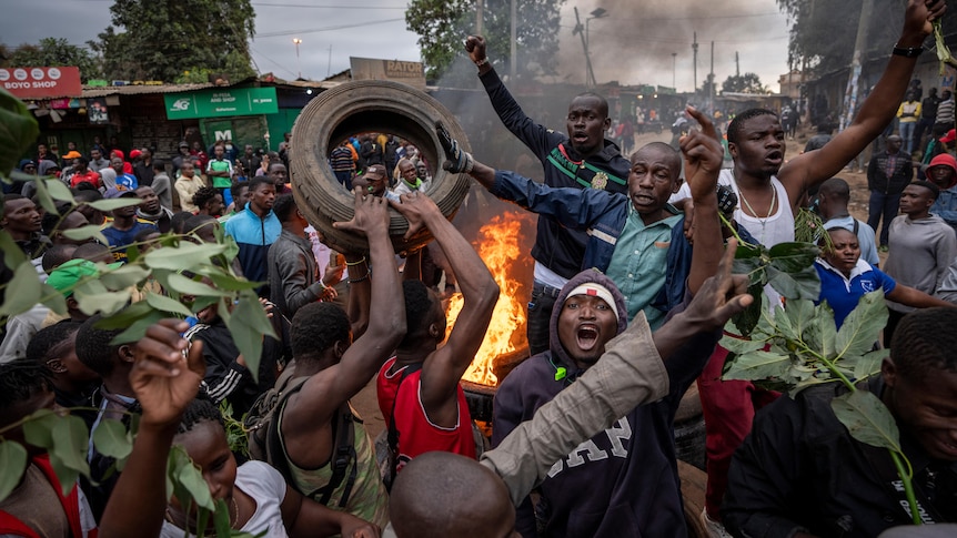 A crowd throw tyres on a fire in the street.