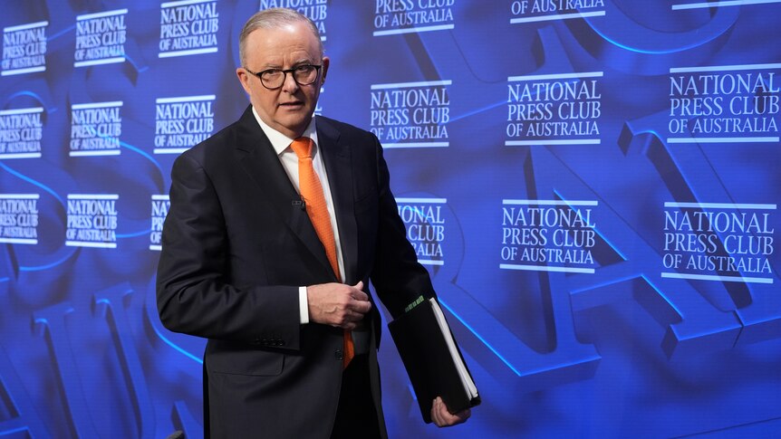 Albanese walks with a folder in hand on the stage of the National Press Club.
