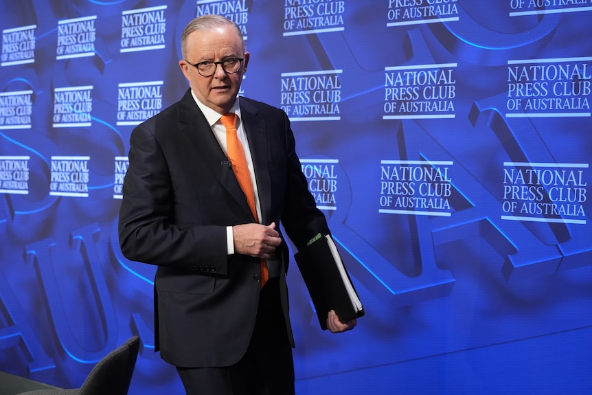 Albanese walks with a folder in hand on the stage of the National Press Club.
