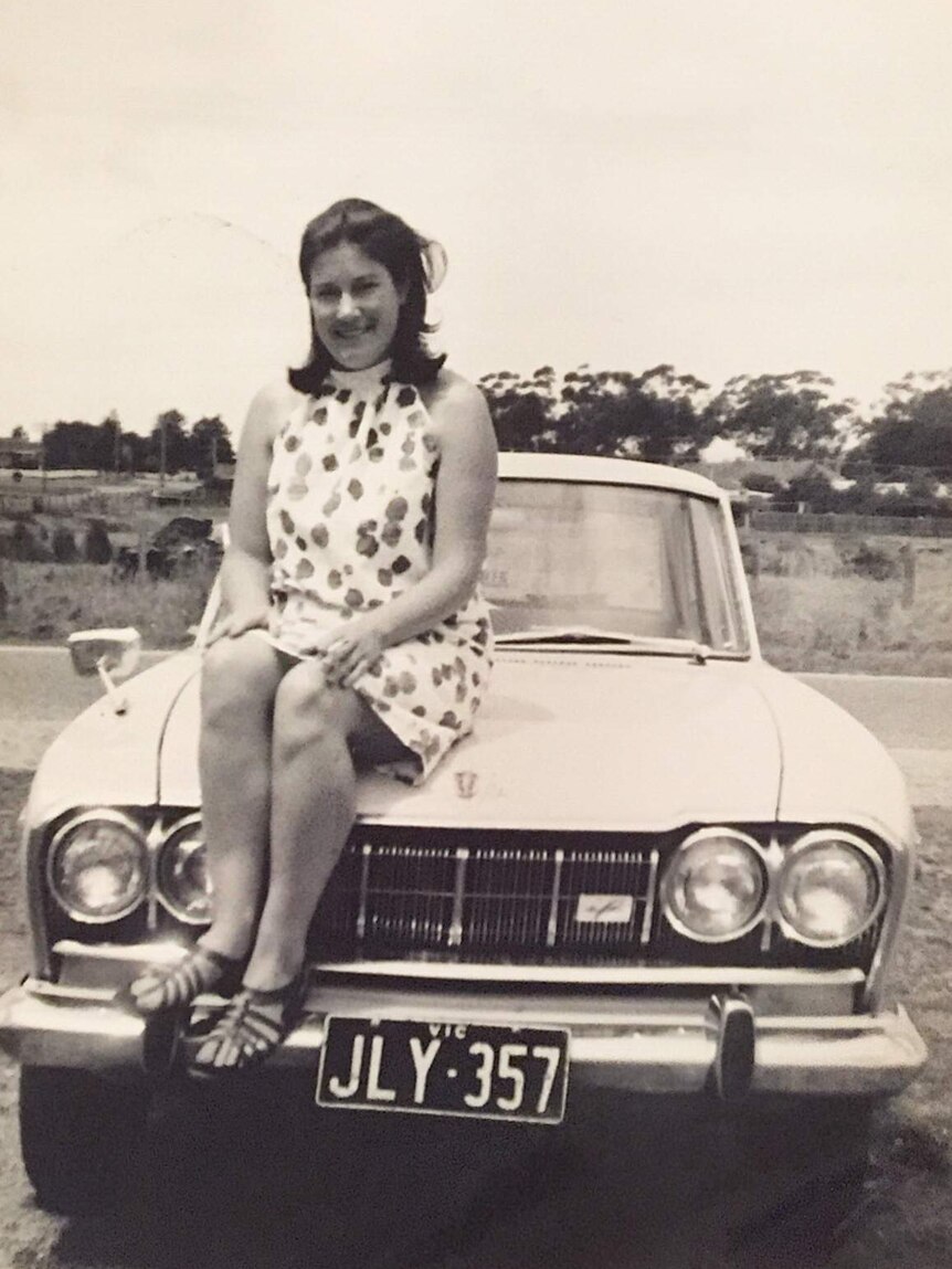 A black and white photo showing Sue McDermott sitting on the bonnet of a car