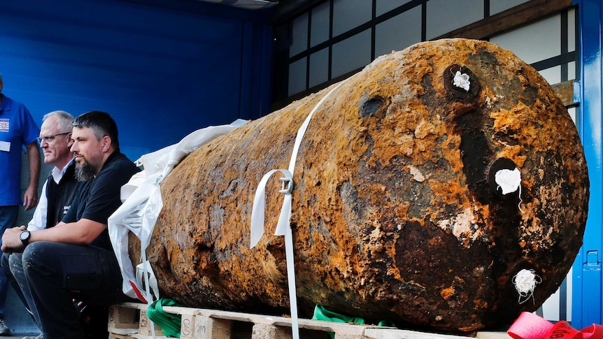 Bomb experts sit next to massive, rusty WWII bomb.