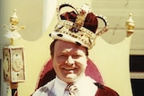 Bert Newton grins as he sits on a throne with a crown, cape and sceptre.