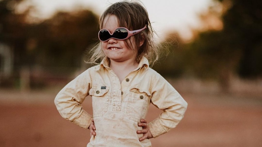 A young child wears sunglasses upside down, while giving a cheeky smile.