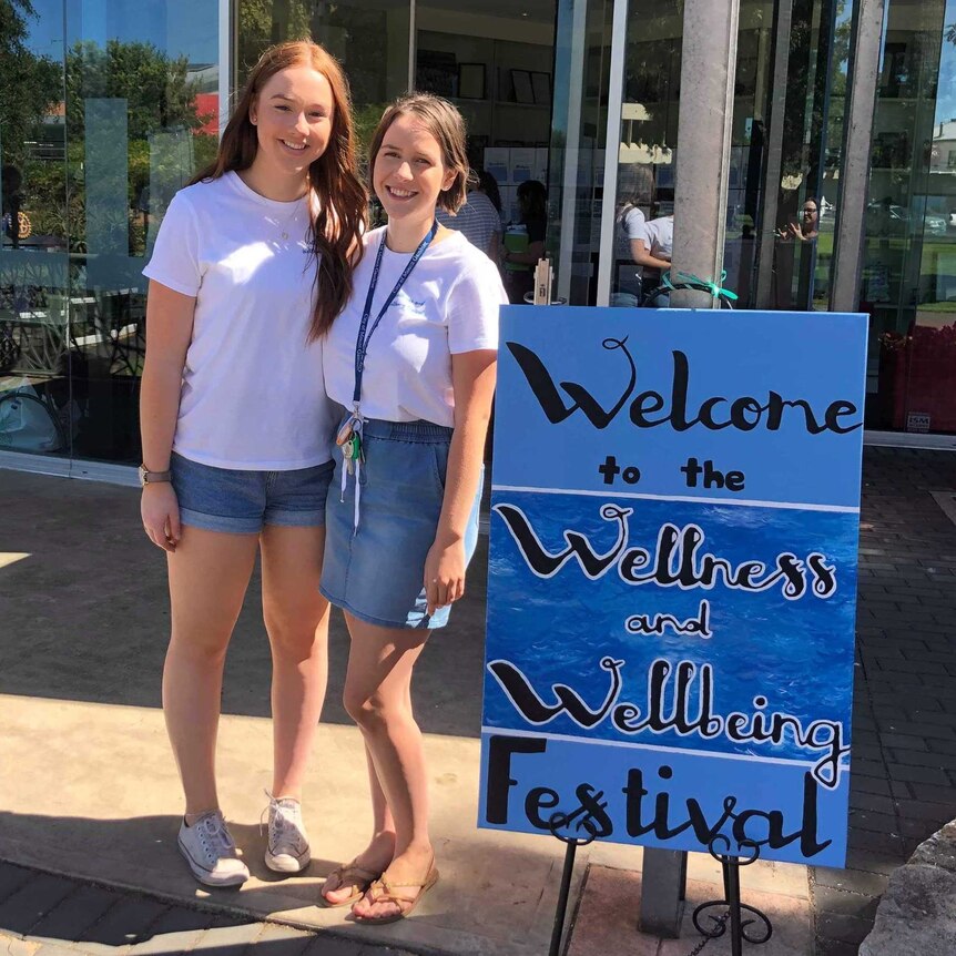 Shanae Coppick, Left, and Tessa Deak, right, stand next to each other next to a welcome sign.