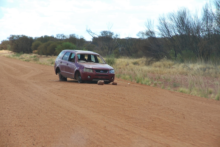 A red suv broken down on a red dirt road 