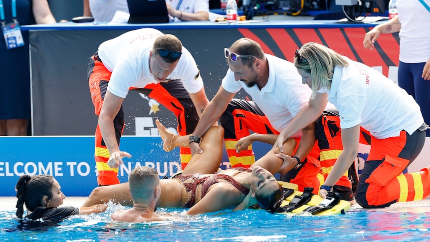An unconscious woman is pulled from a swimming pool by three people and lifted onto a stretcher.