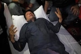 khan on his back ona  stretcher, both arms half raised