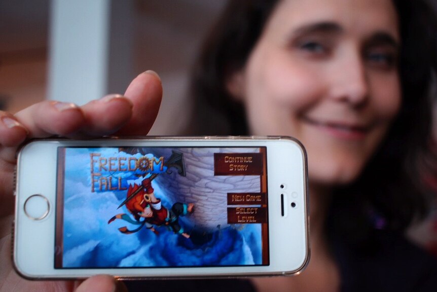 A close-up shot of Stirfire Studios creative director Lisa Rye holding an iPhone with a video game on its screen.
