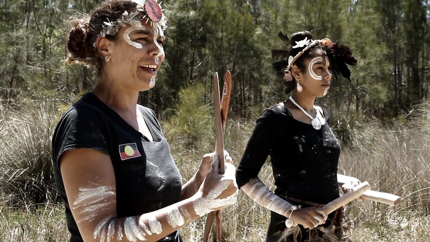 Two indigenous women in face paint practice their traditional dance in bushland next to a river