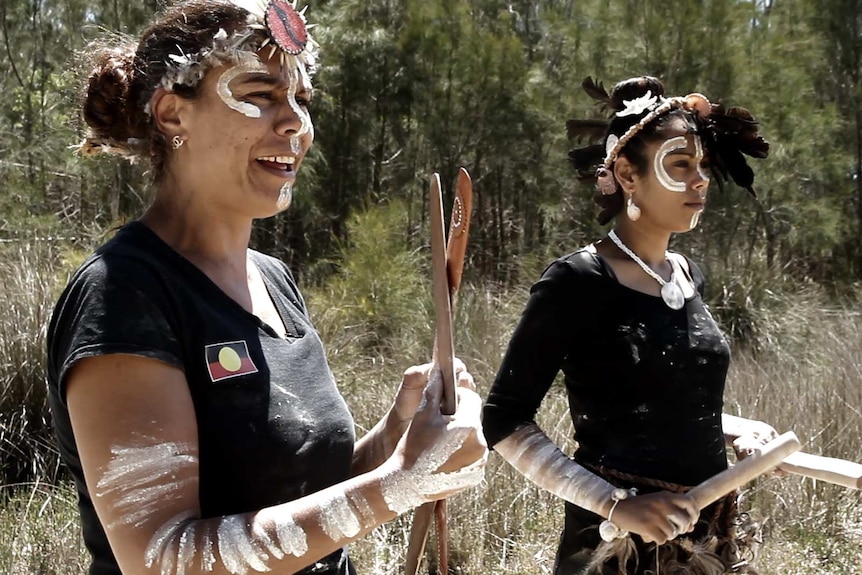 Two indigenous women in face paint practice their traditional dance in bushland next to a river