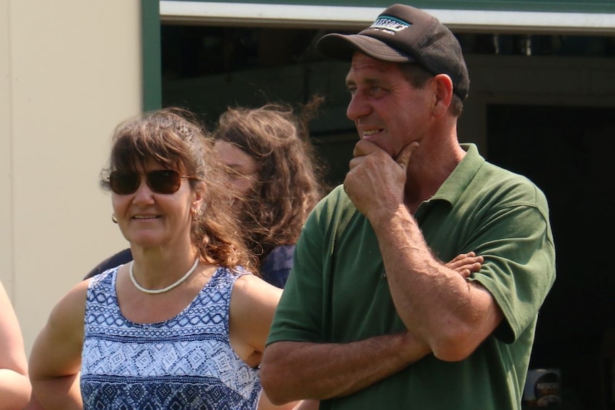 A woman in sunglasses and a singlet stands next to a man wearing a cap and green polo shirt.