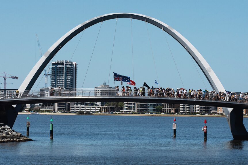 Anti-vax protesters march over the Matagarup Bridge with flags 