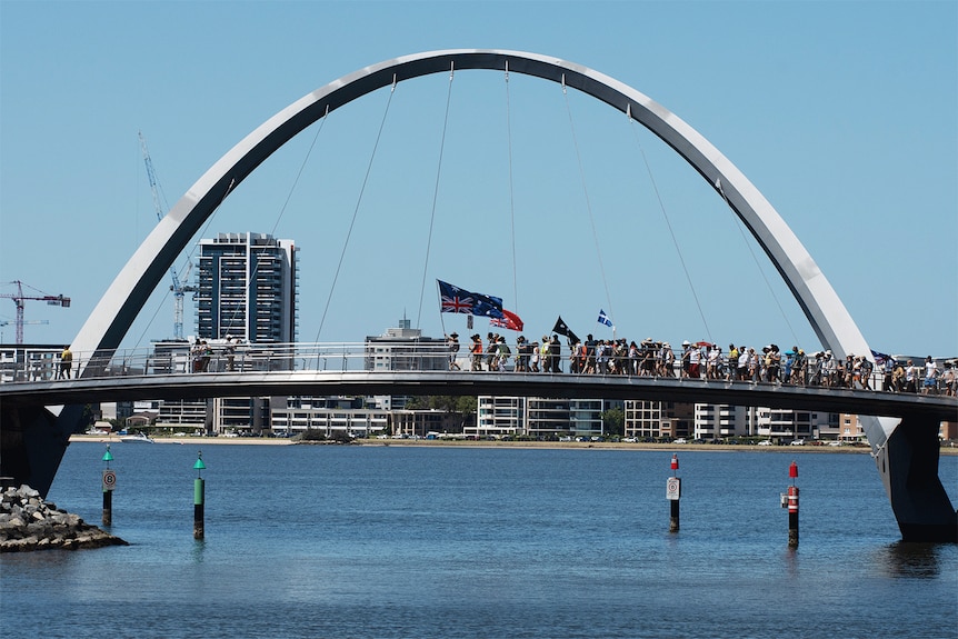 Anti-vax protesters march over the Matagarup Bridge with flags 