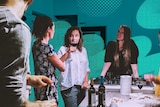 A group of people stand around a kitchen having drinks and making food for a story about why people share in their 30s