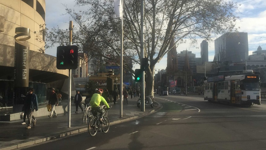 A cyclist wearing bright yellow rides down a city street on a cold morning.