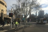 A cyclist wearing bright yellow rides down a city street on a cold morning.