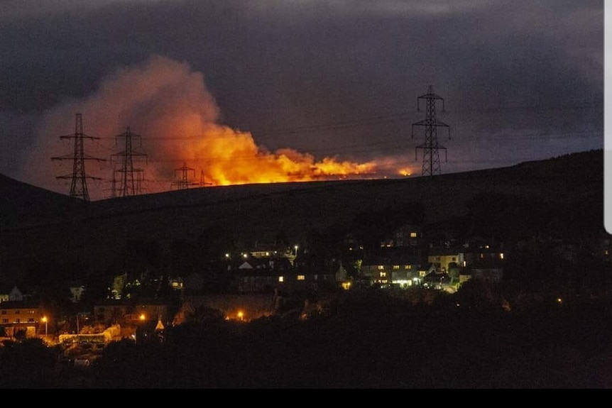 Fire and smoke from the Saddleworth Moor fire burn on a hill above a town