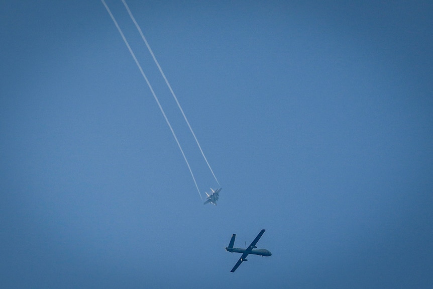 A drone and a jet flying through a clear blue sky 