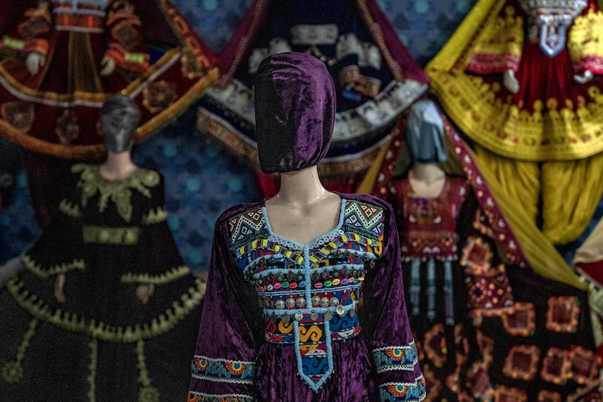 A mannequin in a purple dress beaded with cowrie shells, has a matching purple hood.