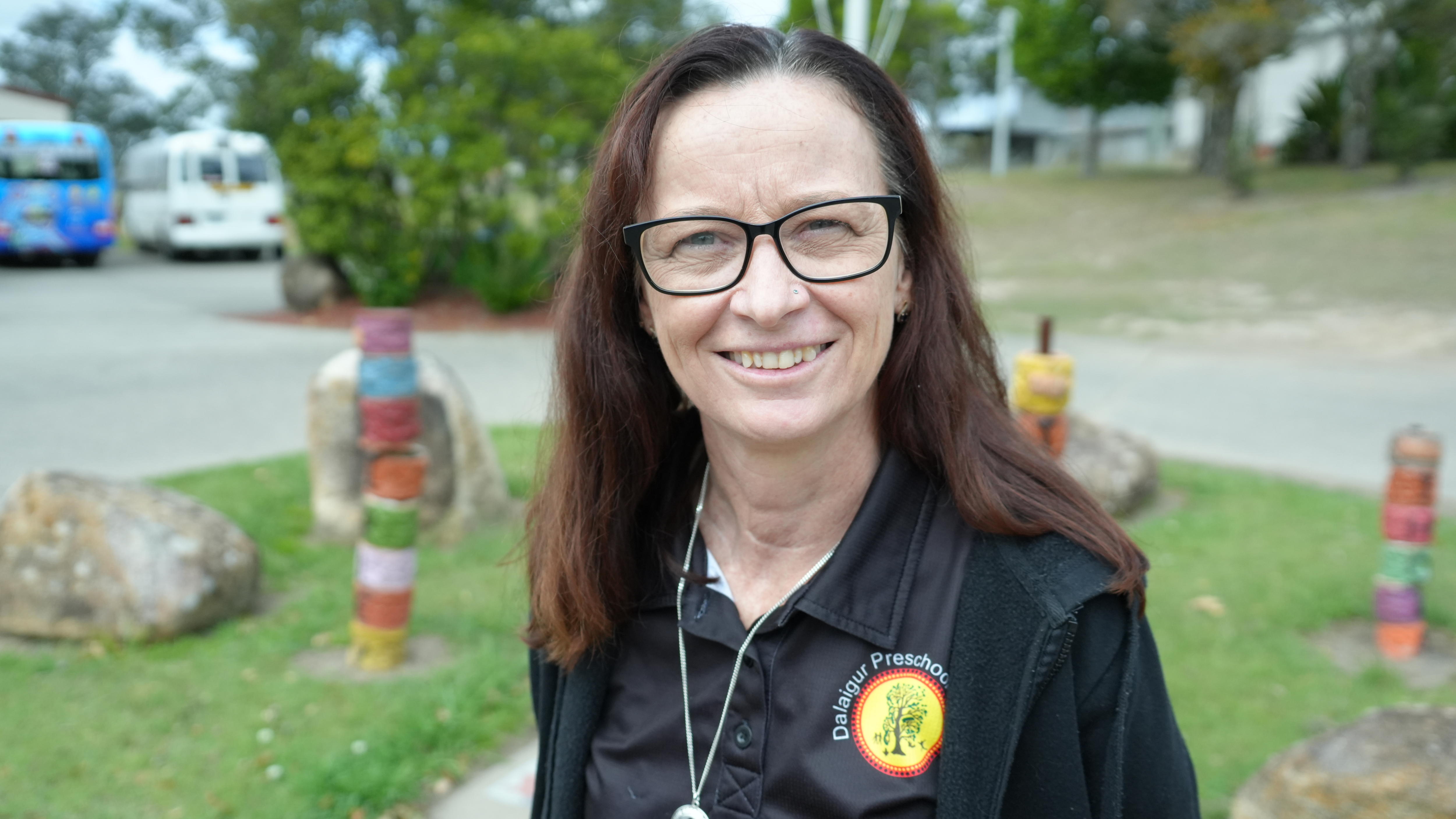 An Indigenous woman standing in front of some totem poles
