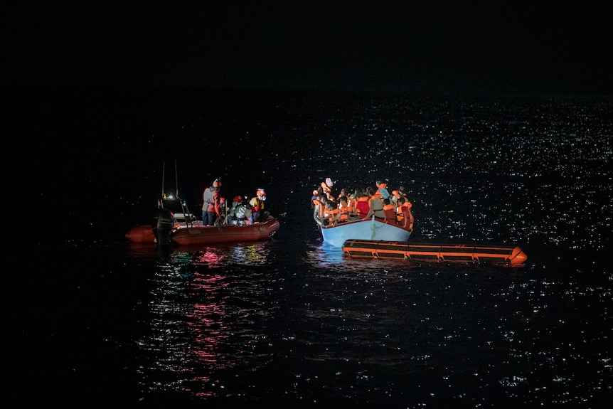 A rescue RIB pulls up alongside the migrant dinghy.