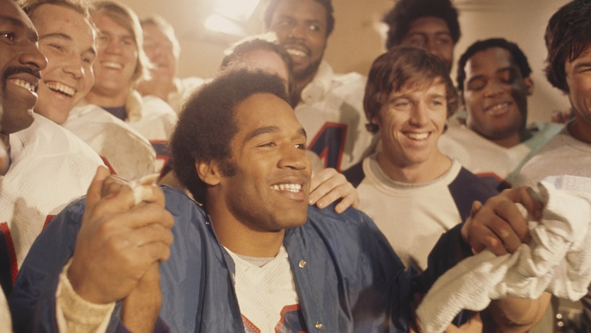 A man surrounded by teammates in his locker room.
