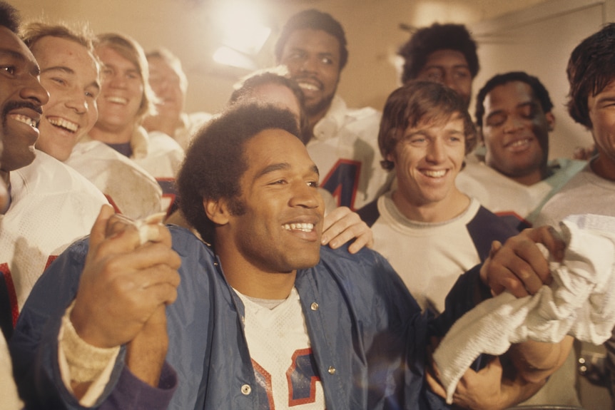 A man surrounded by teammates in his locker room.