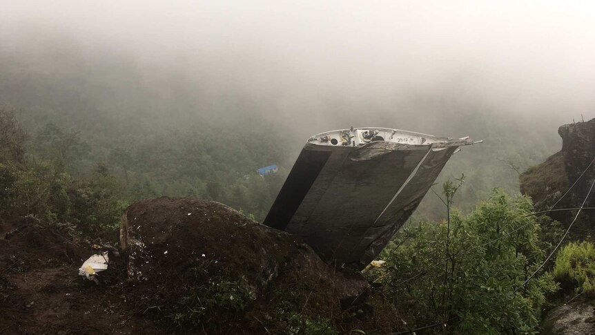 A wrecked plane wing is seen in mountainous terrain.