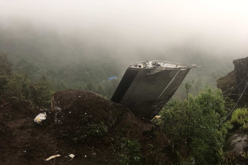 A wrecked plane wing is seen in mountainous terrain.