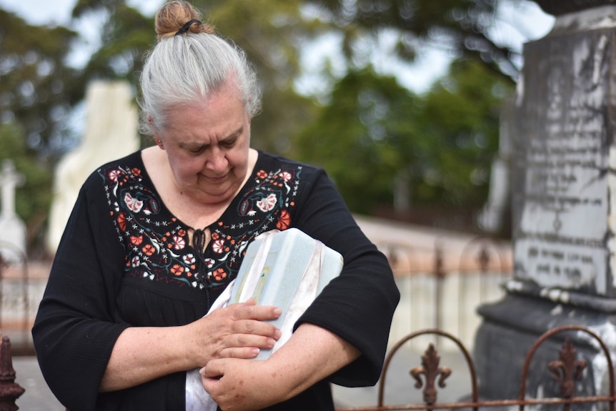 Woman holds an urn containing ashes at a cemetery.