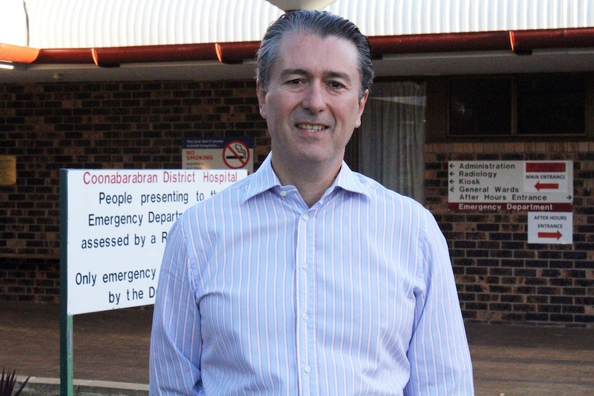 man in collared shirt standing in front of a hospital entrance