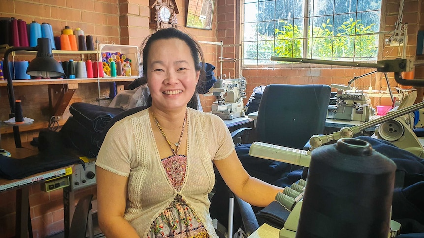 A woman sitting with a sewing maching on a table and smiling to camera