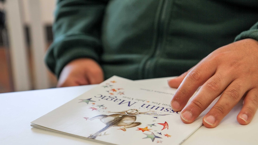 A man's hand rests on a copy of a child's book.