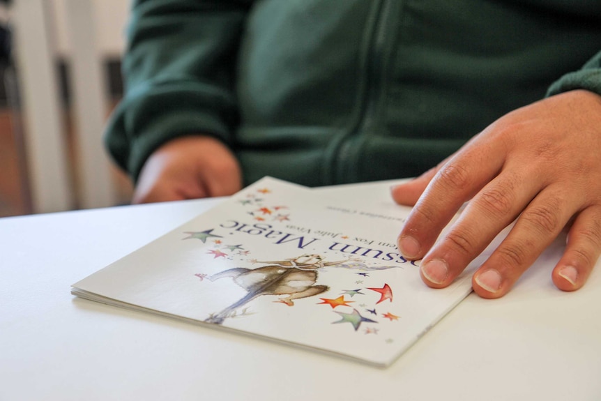 A man's hand rests on a copy of a child's book.