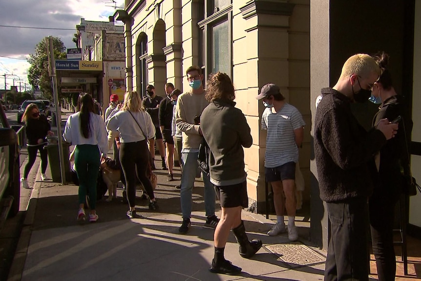 People line up for takeaway drinks outside a pub on a sunny day.