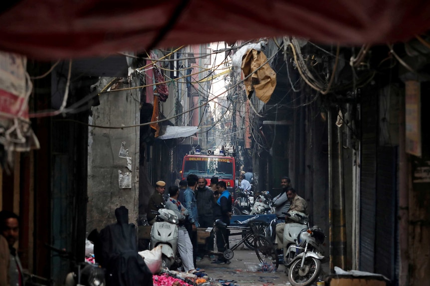 A fire engine drives through a narrow alleyway surrounded by people and electrical wires