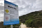 A sign posted at the entrance to a popular beach warning visitors about dangers.