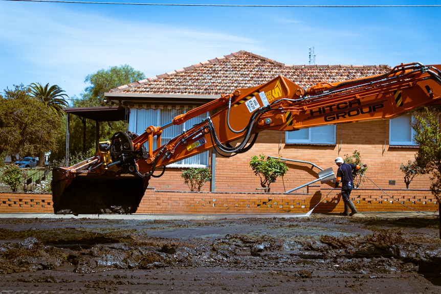 Le bras d'une grande excavatrice se prépare à ramasser de la boue à l'extérieur d'une maison