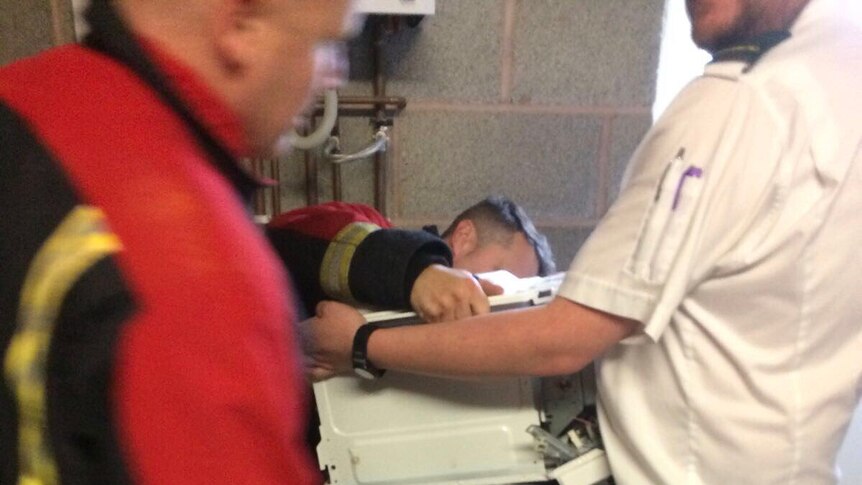 Firefighters try to remove a microwave from a man's head.