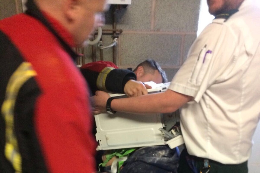 Firefighters try to remove a microwave from a man's head.