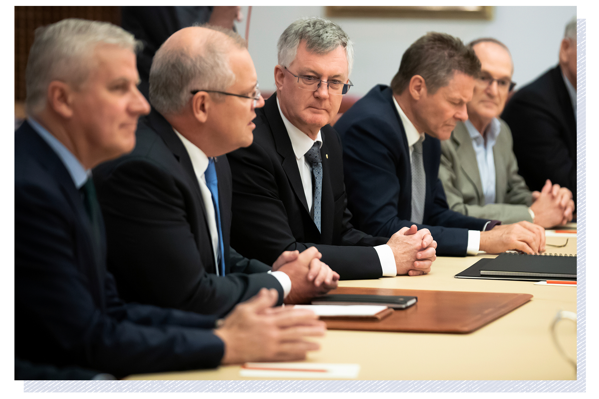 Martin Parkinson sits beside Scott Morrison at a table, flanked by other men, and looks towards him as Morrison speaks.