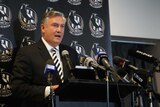 Eddie McGuire standing at a lectern in front of a banner with magpies logo.
