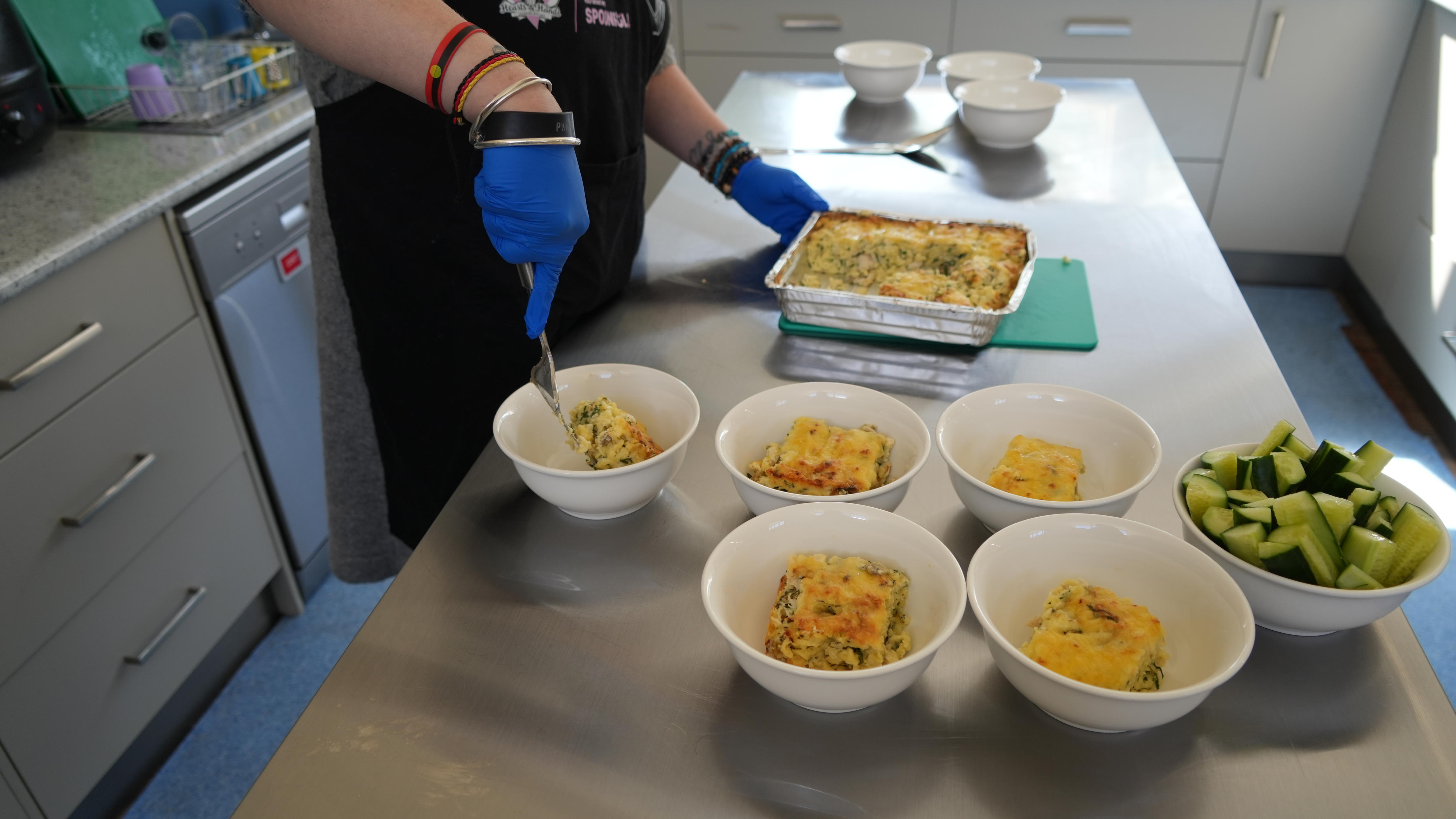 A woman plates up a pasta bake dish with zucchini sticks.