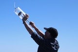 A man holds a clear canister up above his head.