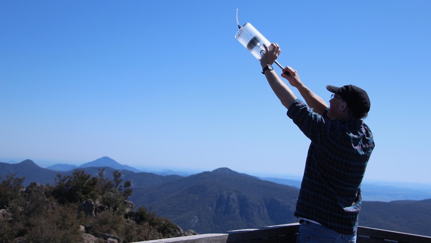 A man holds a clear canister up above his head.