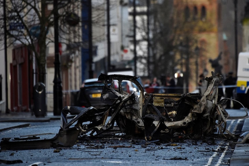 The burnt metal remnants of a car in which a bomb was detonated sits over debris scattered across a street.