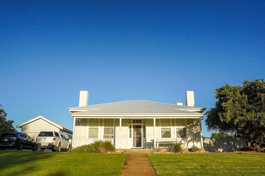 A white weatherboard cottage sits atop of a gently rolling lawn.